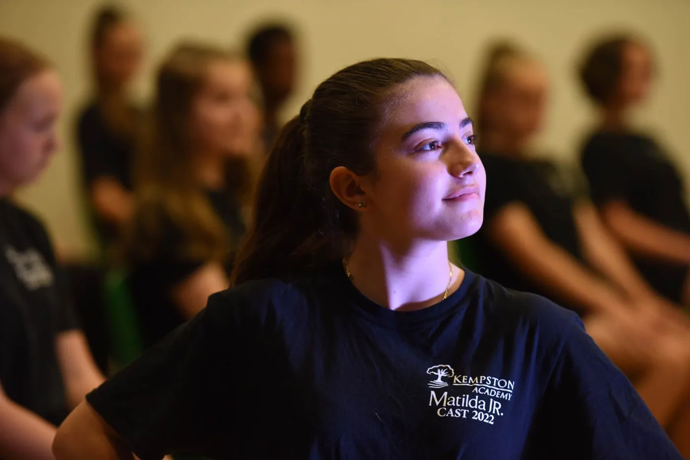 A Kempston Academy student in a black Matilda Jr. Cast 2022 T-shirt, with other students seated behind